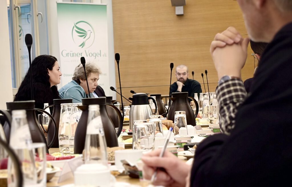 Diskussionsrunde beim parlamentarischen Frühstück von Grüner Vogel e.V. im Bundestag, mit Mikrofonen und Konferenztisch im Vordergrund.